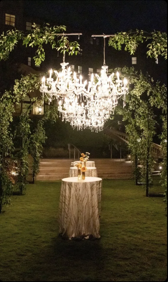 Crystal chandelier suspended within a lush greenery arch over a cocktail table