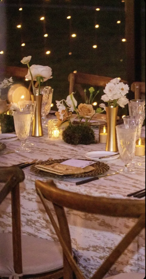 Tablescape detail with gold bud vases, white garden roses, votives, and crystal glassware